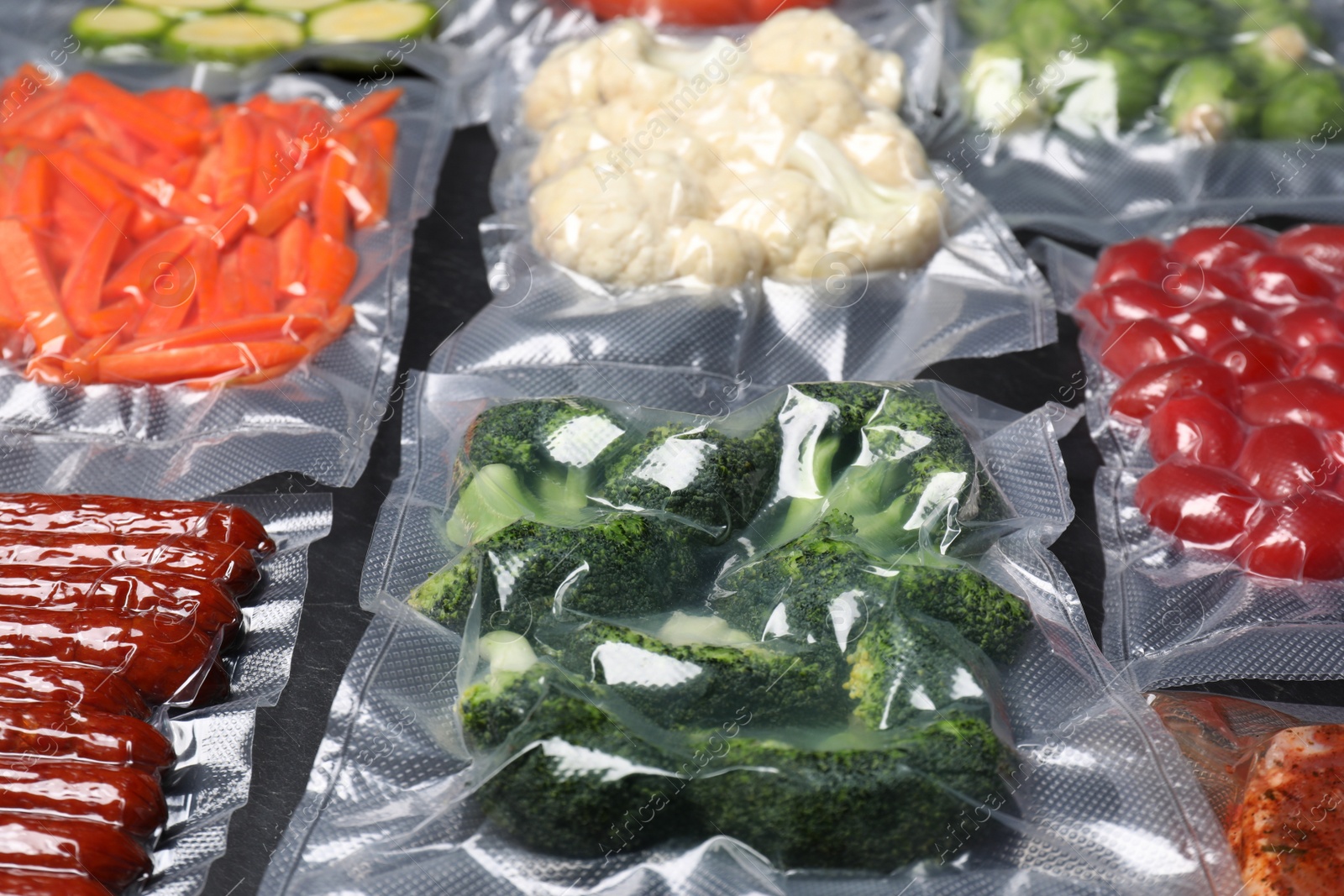 Photo of Many different food in vacuum packings on dark grey table, closeup