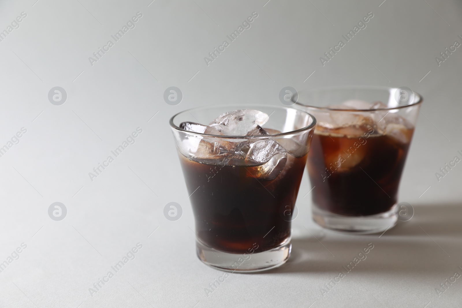 Photo of Refreshing iced coffee in glasses on grey background. Space for text