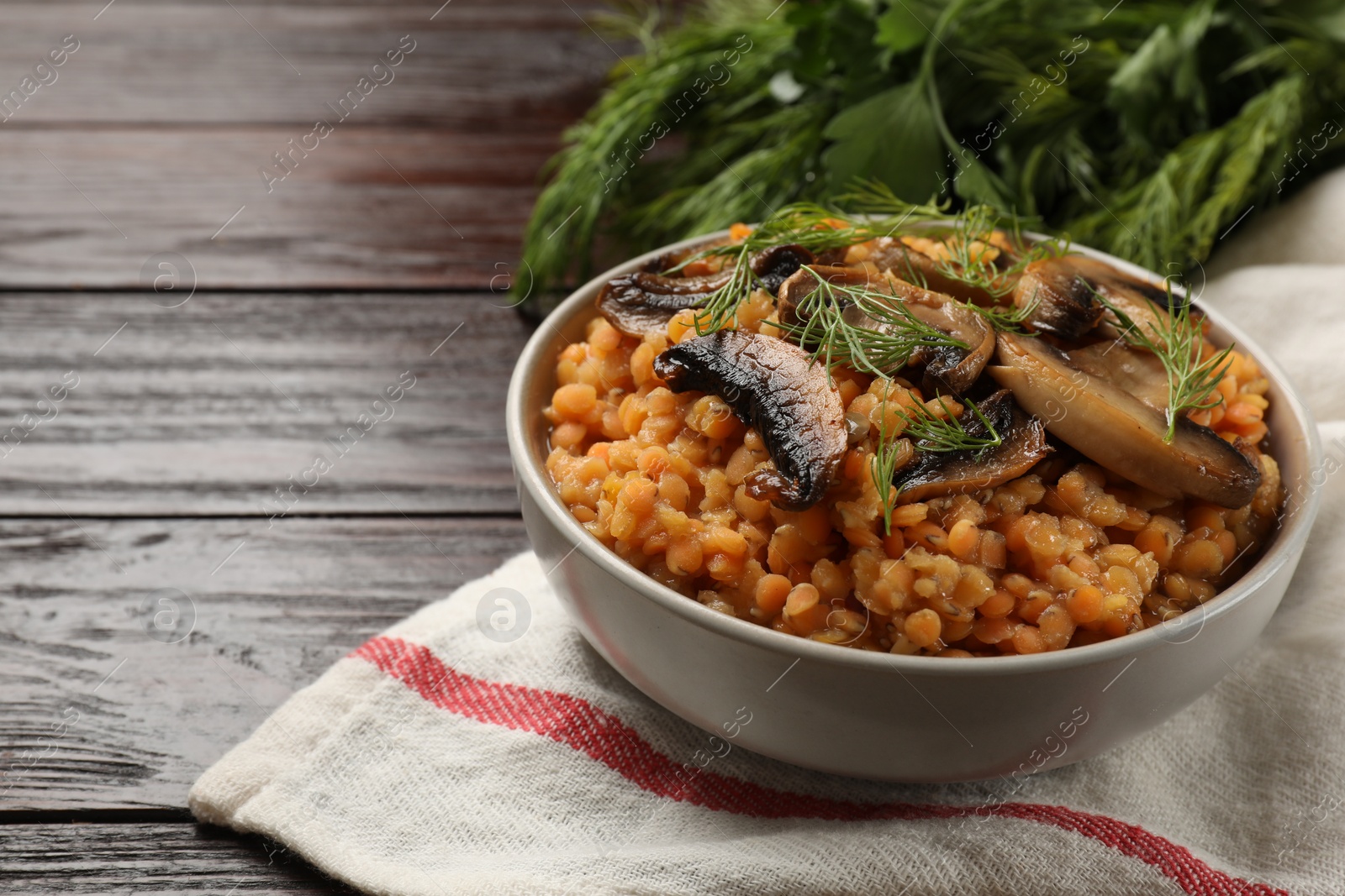 Photo of Delicious red lentils with mushrooms and dill in bowl on wooden table, closeup. Space for text