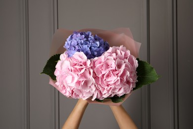 Photo of Woman with bouquet of beautiful hortensia flowers near grey wall, closeup