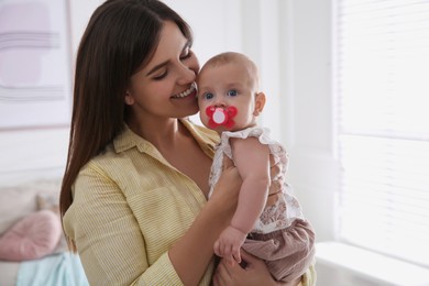 Photo of Happy mother holding her cute little baby with pacifier at home