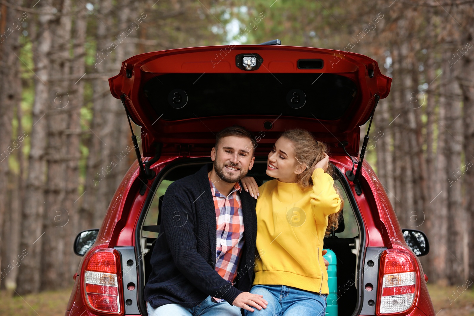 Photo of Young couple with suitcase sitting in car trunk on forest road