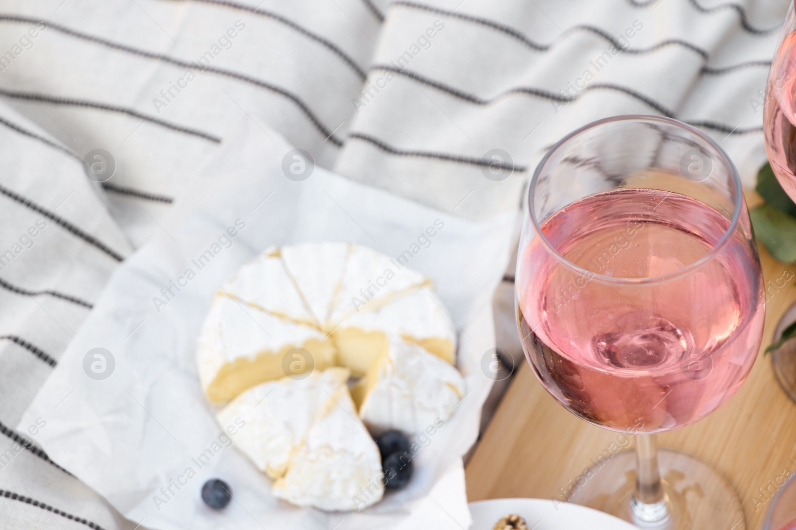 Photo of Glass of delicious rose wine and food on white picnic blanket, closeup