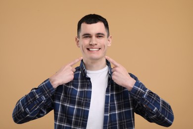 Photo of Handsome young man showing his clean teeth on beige background