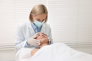 Photo of Dermatologist in medical mask examining patient`s face in clinic