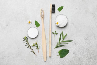Photo of Bamboo toothbrushes, flowers and herbs on light grey table, flat lay