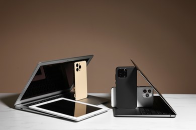 Many different modern gadgets on white table against brown background