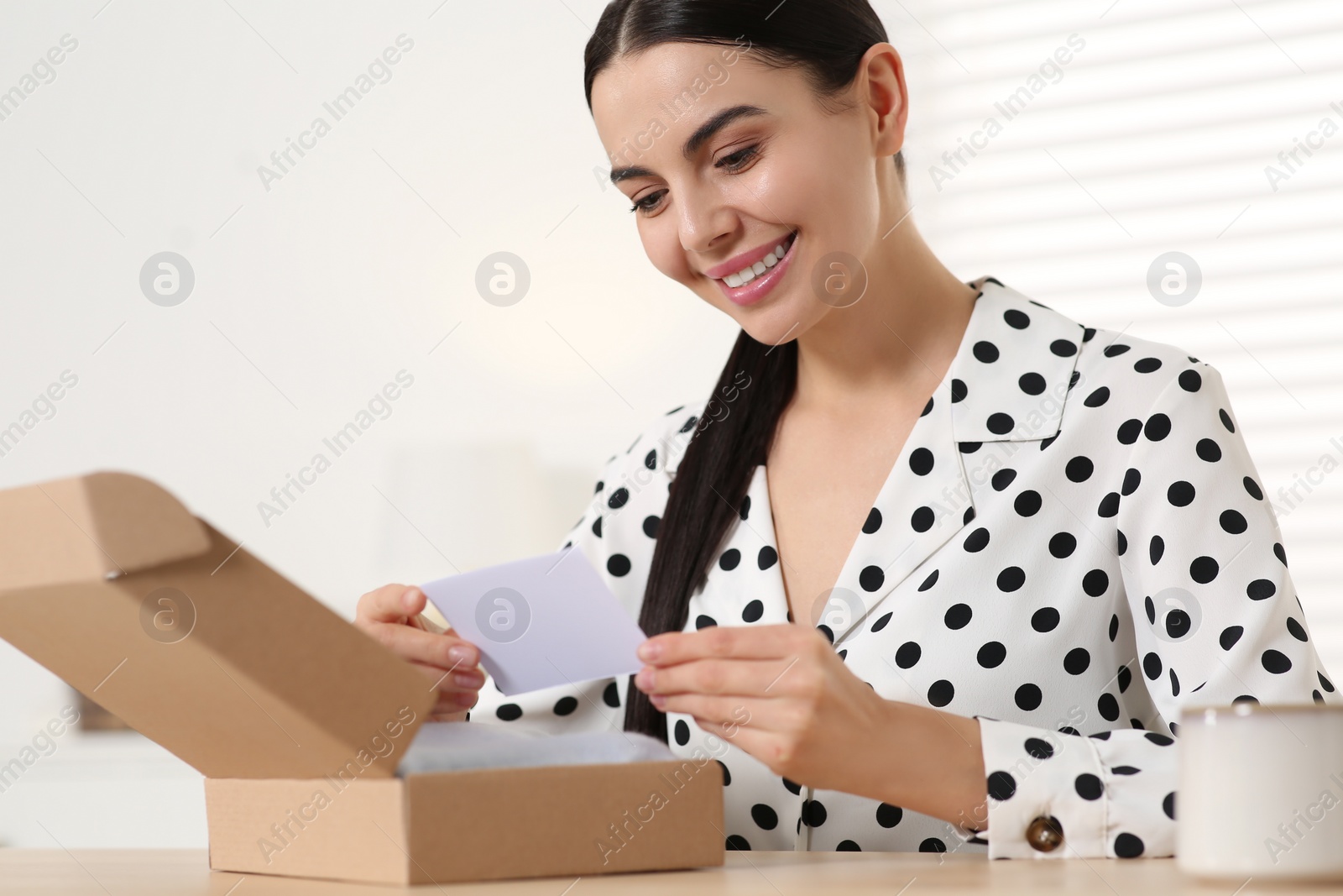 Photo of Happy woman holding greeting card near parcel with Christmas gift at home