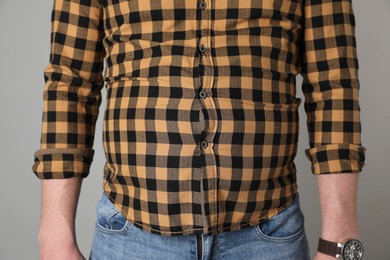 Overweight man in tight shirt on grey background, closeup