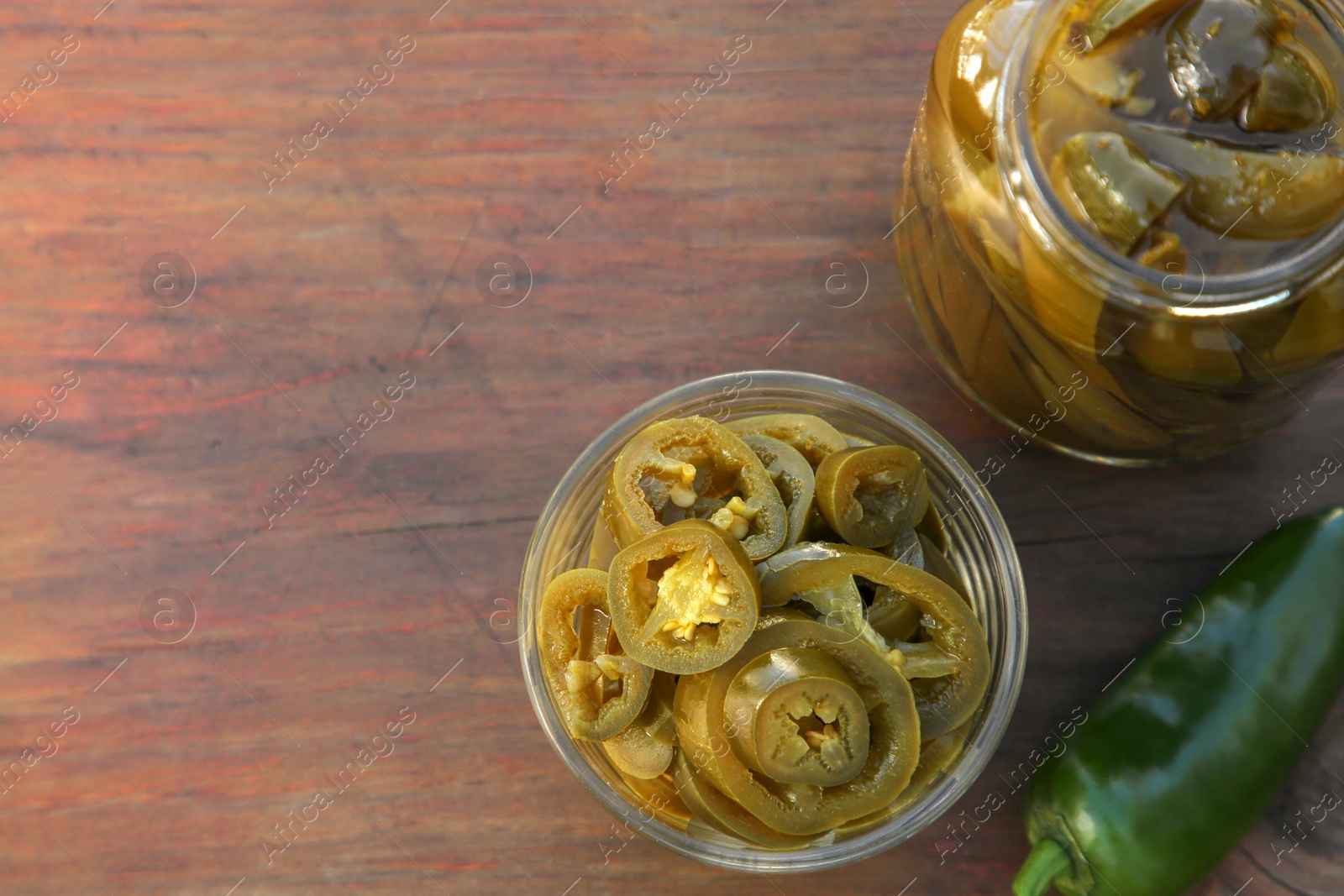 Photo of Fresh and pickled green jalapeno peppers on wooden table, flat lay. Space for text