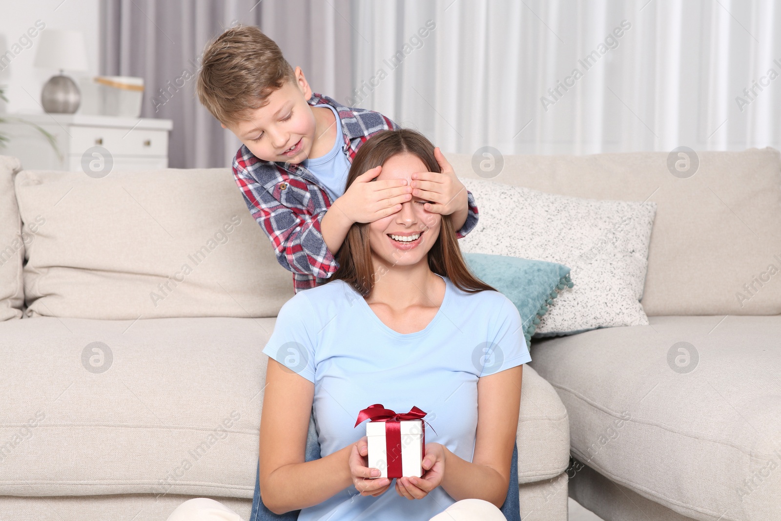 Photo of Little boy presenting his mother with gift on sofa at home