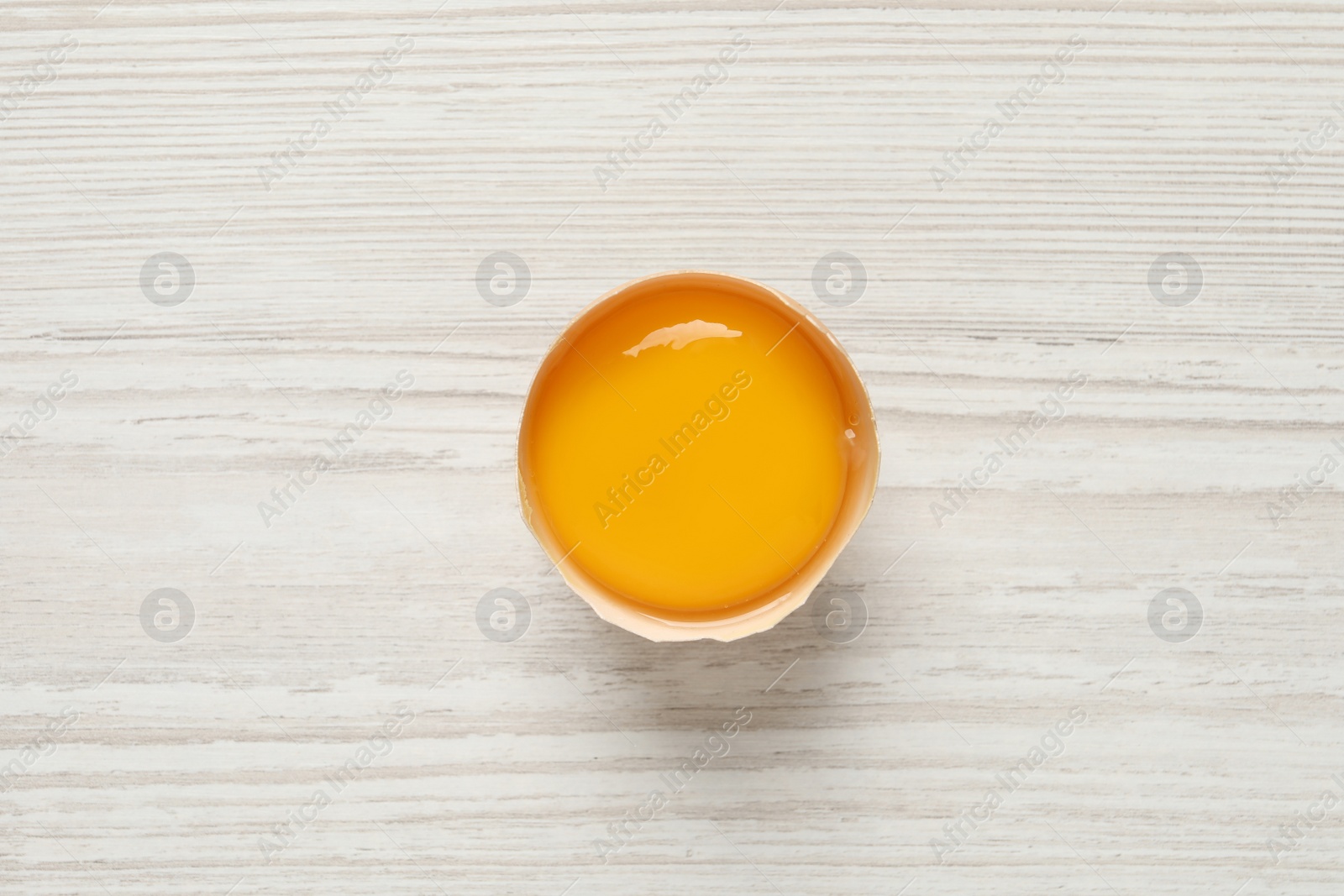 Photo of Raw yolk in broken chicken eggshell on white wooden table, top view