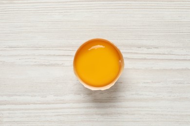 Photo of Raw yolk in broken chicken eggshell on white wooden table, top view