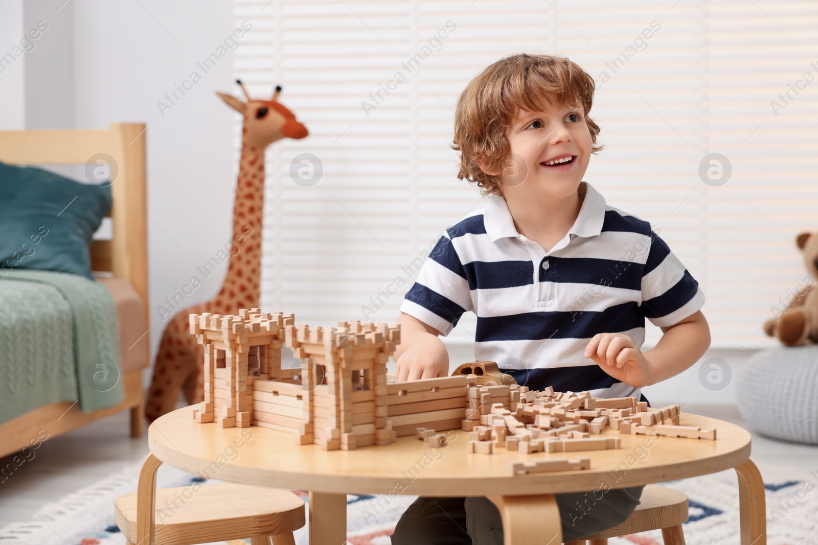 Photo of Cute little boy playing with wooden construction set at table in room. Child's toy