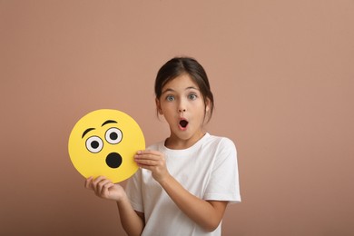 Photo of Emotional little girl holding face with shocked emoji on pale pink background