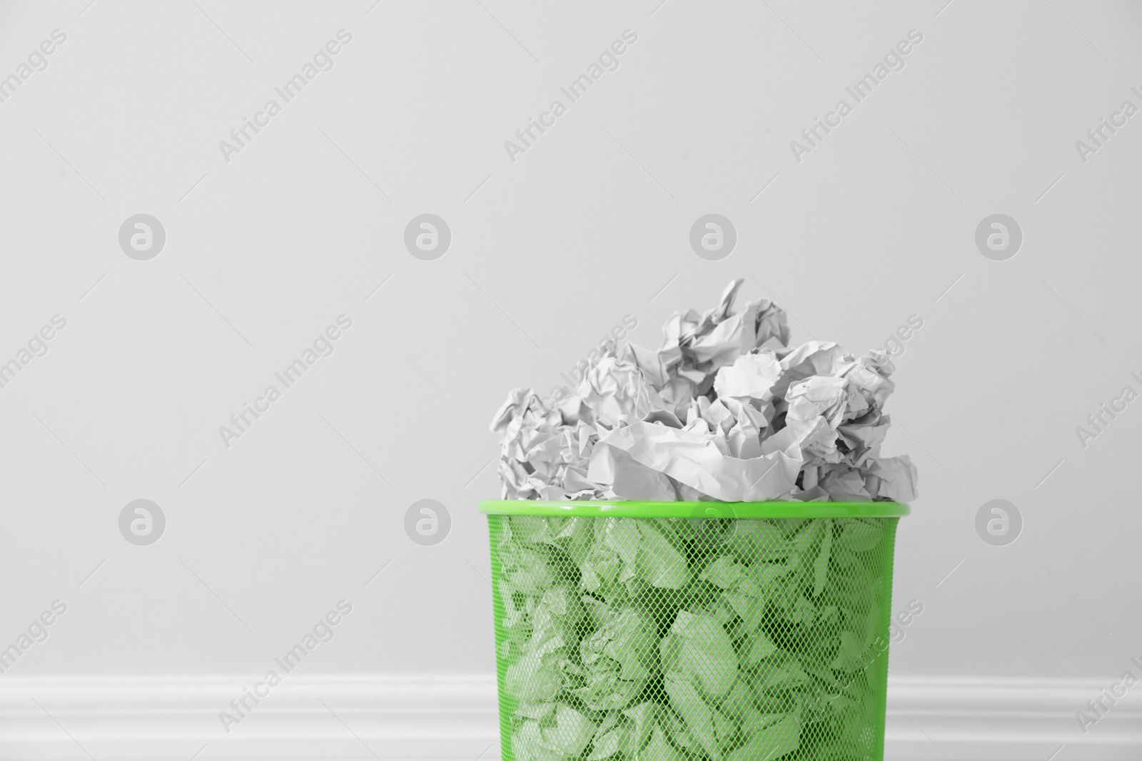 Photo of Metal bin with crumpled paper against light background, space for text