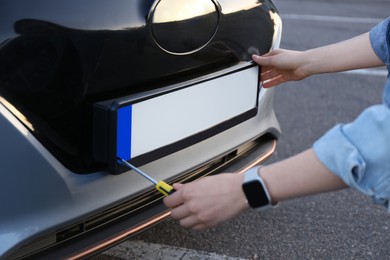 Woman with screwdriver installing vehicle registration plate to car outdoors, closeup