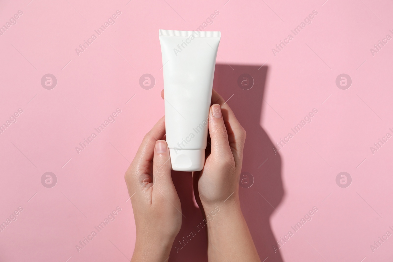 Photo of Woman with tube of hand cream on pink background, top view