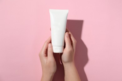 Woman with tube of hand cream on pink background, top view