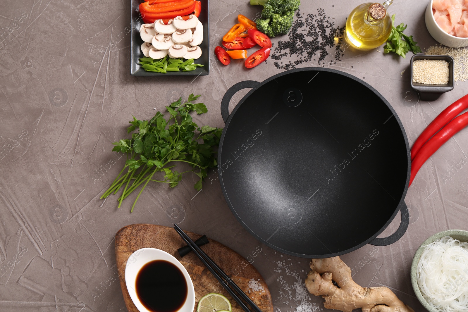 Photo of Wok, chopsticks and different products on grey textured table, flat lay. Space for text