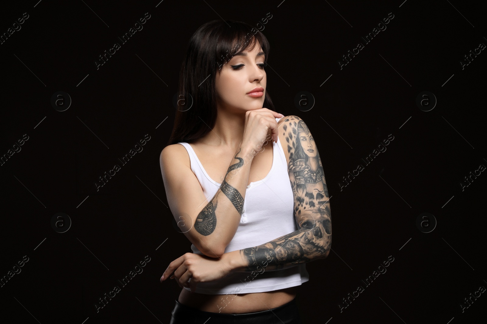 Photo of Beautiful woman with tattoos on arms against black background