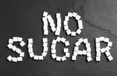 Photo of Phrase No Sugar made of refined cubes on black table, flat lay