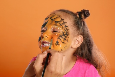 Photo of Artist painting face of little girl on orange background