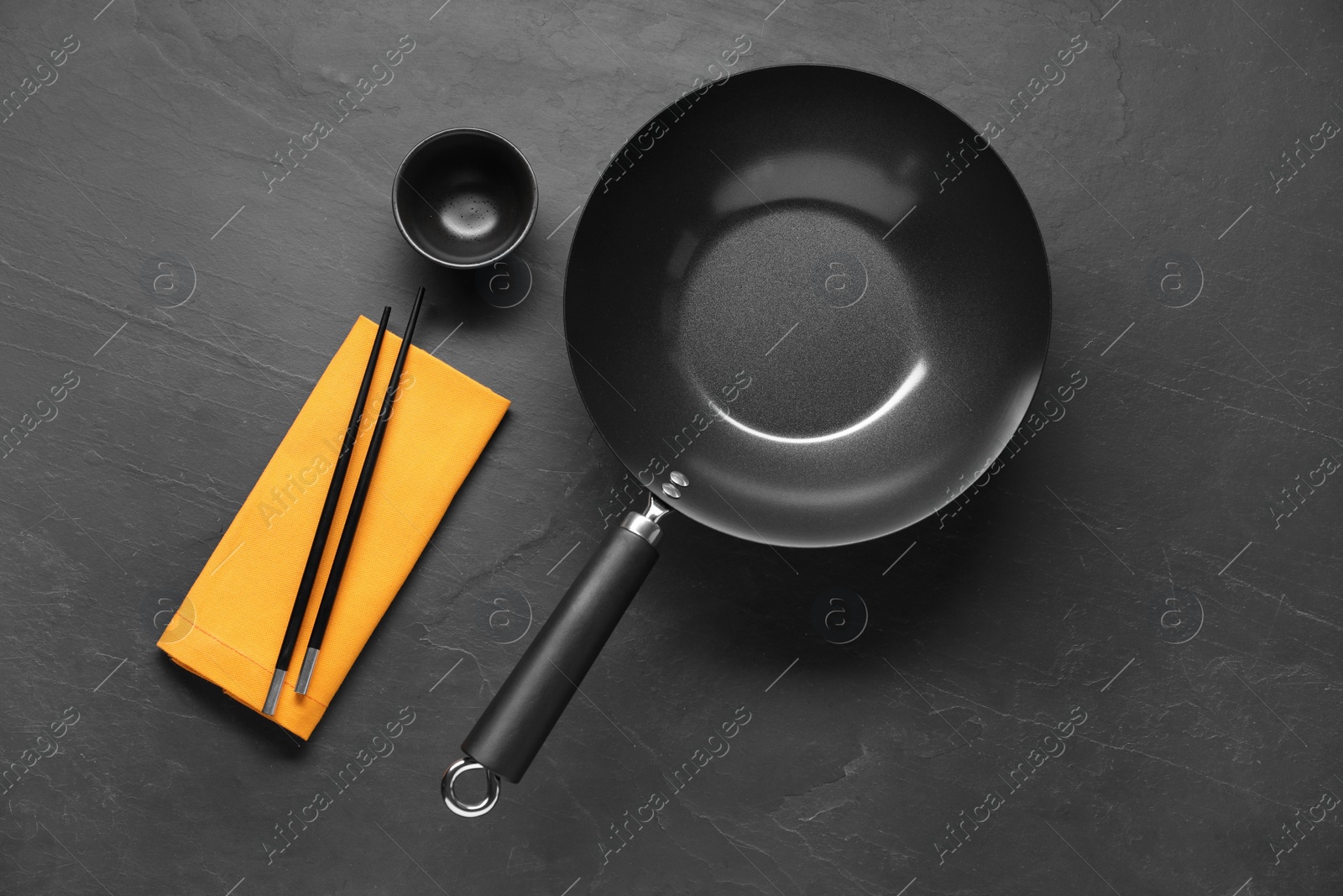 Photo of Empty iron wok, sauce bowl and chopsticks on black table, flat lay