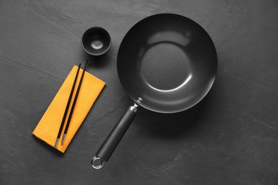 Photo of Empty iron wok, sauce bowl and chopsticks on black table, flat lay