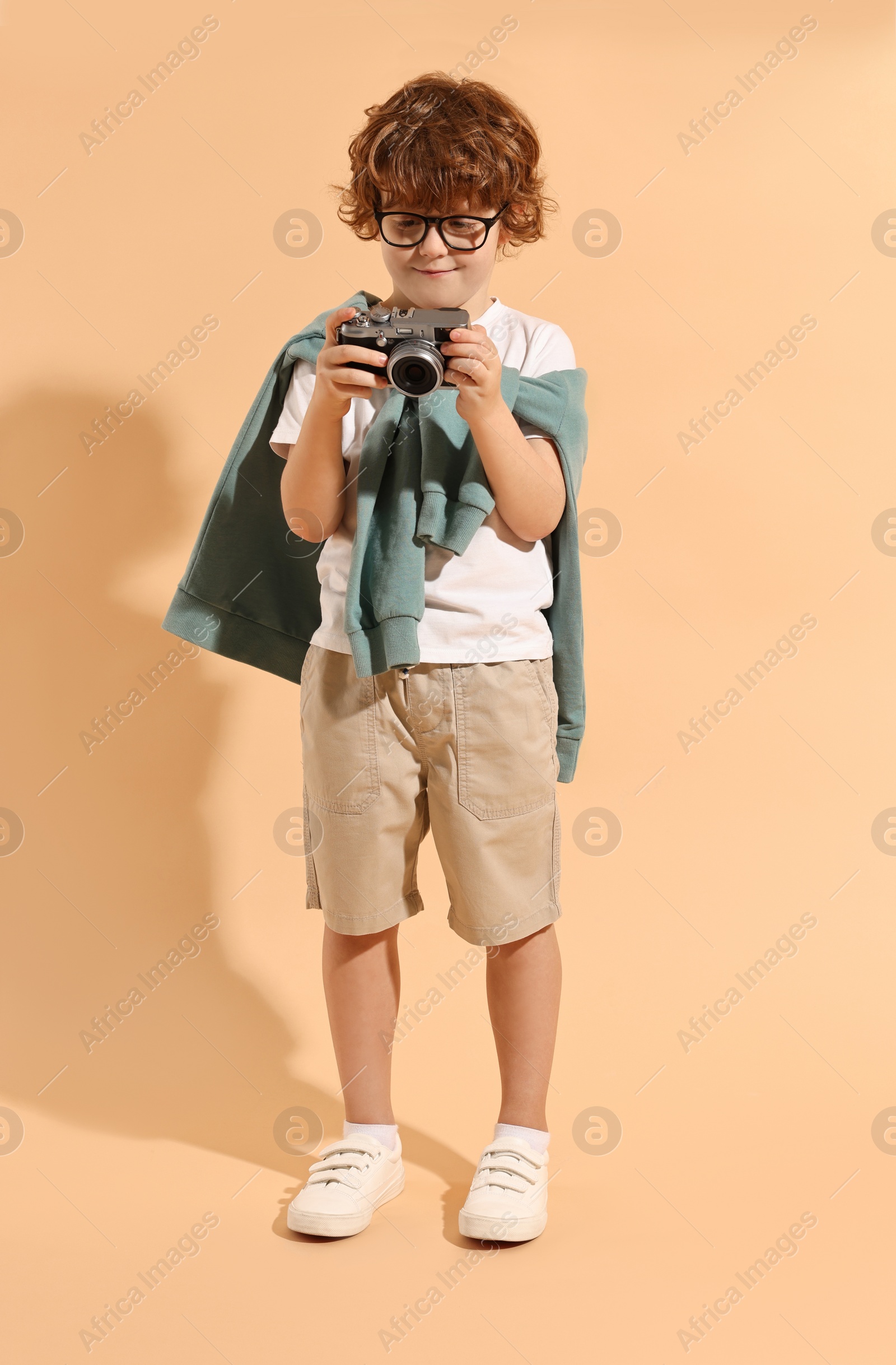 Photo of Fashion concept. Stylish boy with vintage camera on pale orange background