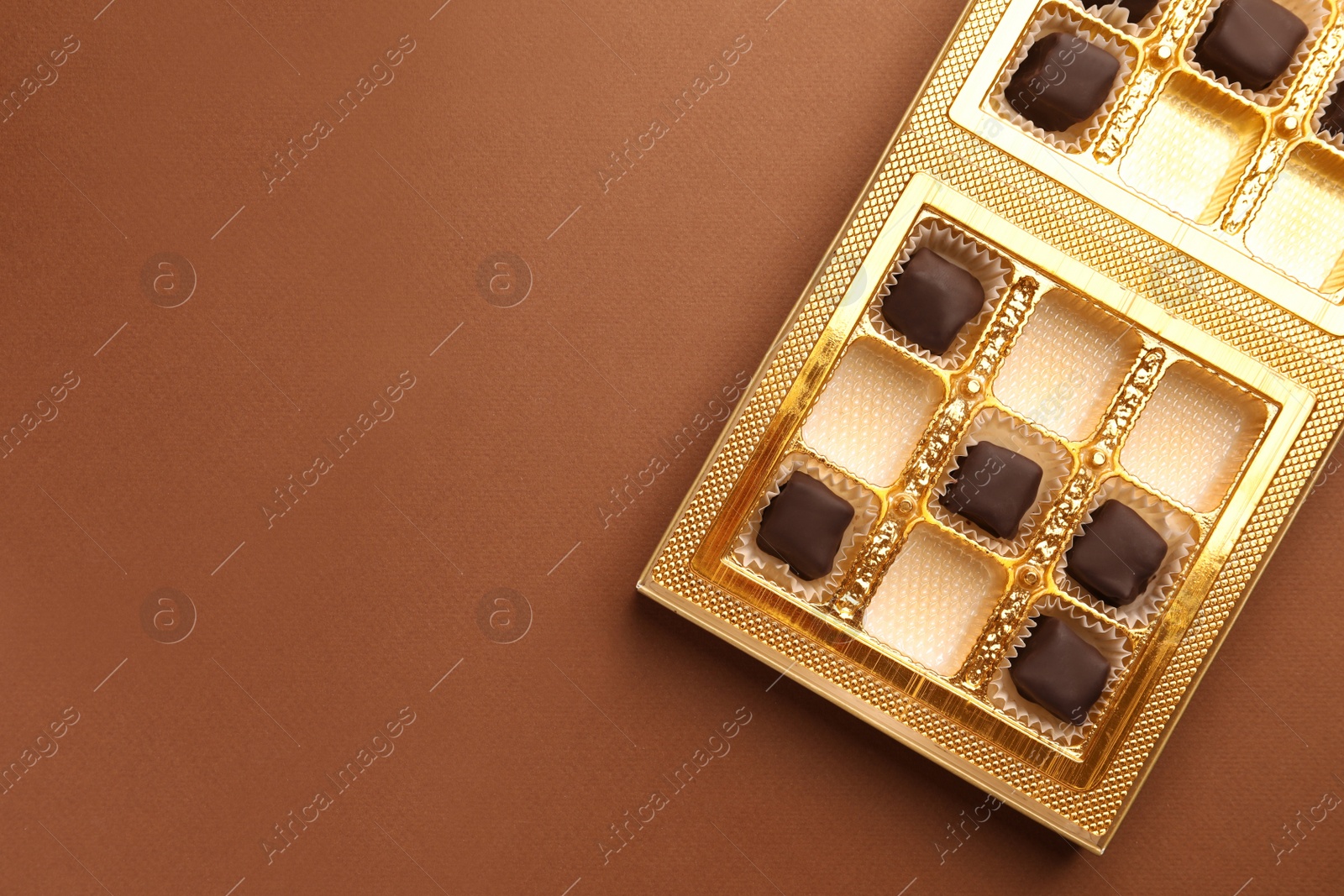 Photo of Partially empty box of chocolate candies on brown background, top view. Space for text