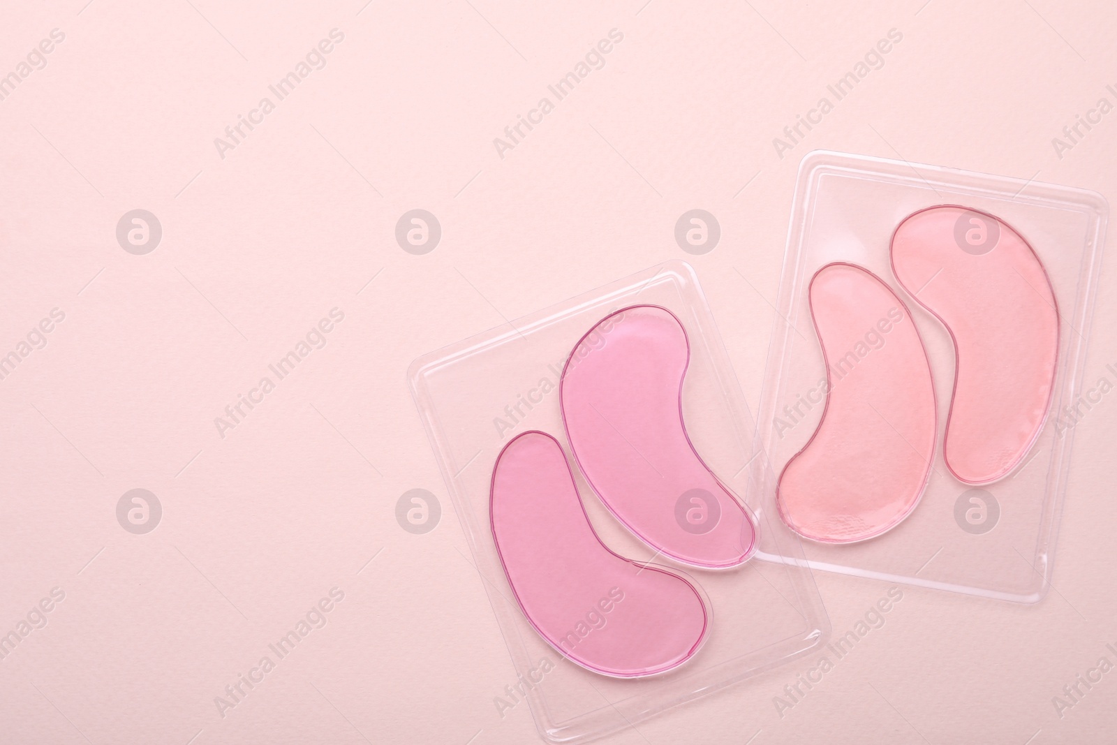 Photo of Packages with under eye patches on light pink background, flat lay. Space for text