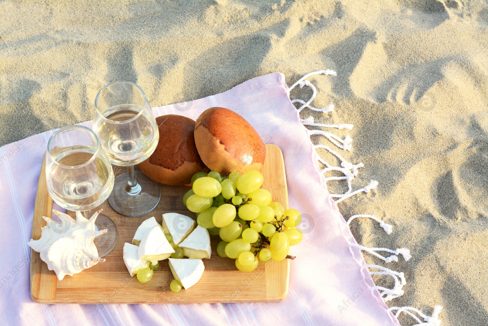 Photo of Glasses with white wine and snacks for beach picnic on sand outdoors