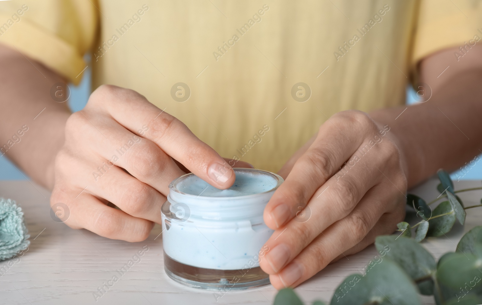 Photo of Woman with jar of body cream at white wooden table, closeup