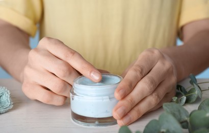 Woman with jar of body cream at white wooden table, closeup