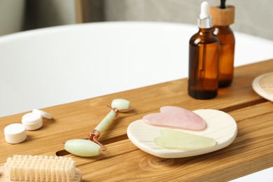 Photo of Jade and rose quartz gua sha tools, natural face roller with cosmetic products on wooden caddy in bathroom