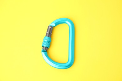 Photo of One light blue carabiner on yellow background, top view