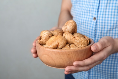 Photo of Woman holding bowl with dried figs on light background, space for text. Healthy fruit