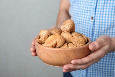 Woman holding bowl with dried figs on light background, space for text. Healthy fruit