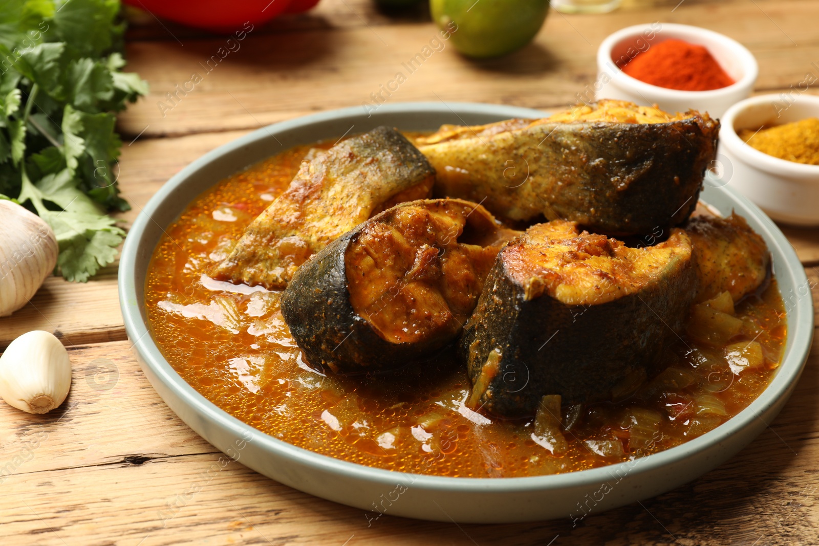 Photo of Tasty fish curry and ingredients on wooden table, closeup. Indian cuisine