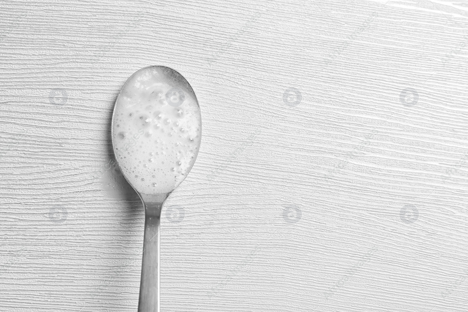 Photo of Chemical reaction of vinegar and baking soda in spoon on table, top view. Space for text