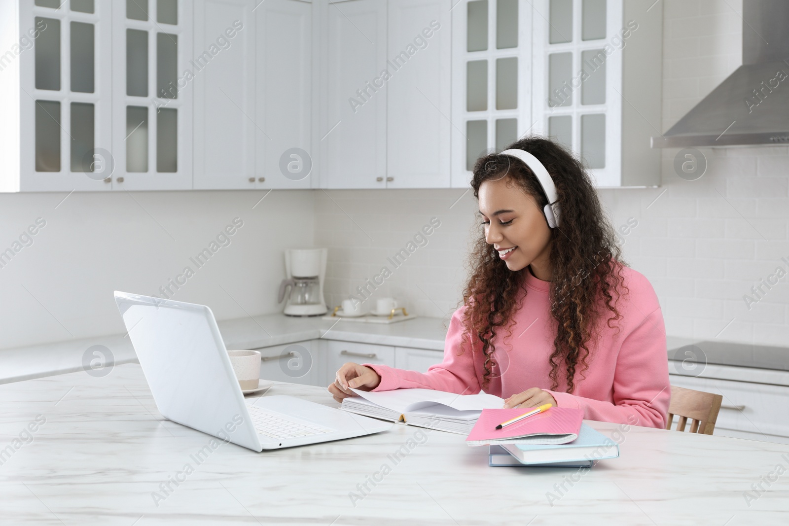 Photo of African American woman with modern laptop and headphones studying in kitchen. Distance learning