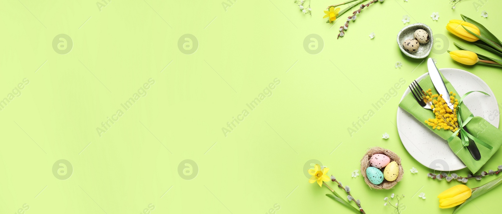 Image of Festive Easter table setting with eggs and floral decor on green background, flat lay. Space for text