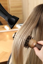 Hairdresser blow drying client's hair in salon, closeup