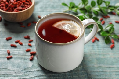 Photo of Healthy goji tea with lemon in cup on blue wooden table