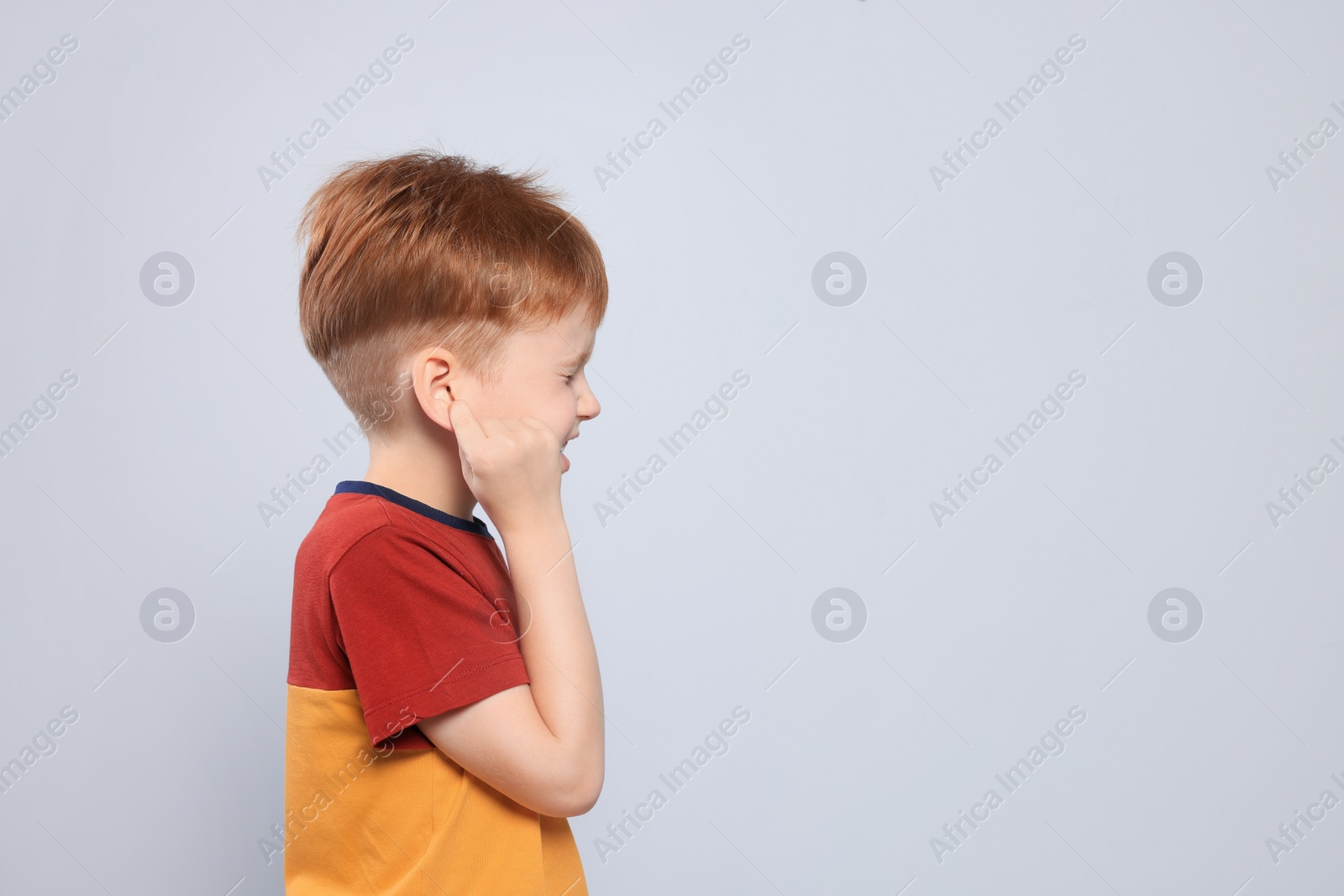 Photo of Little boy suffering from ear pain on light grey background. Space for text