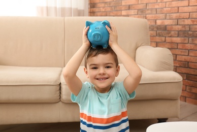Photo of Little boy with piggy bank at home. Saving money