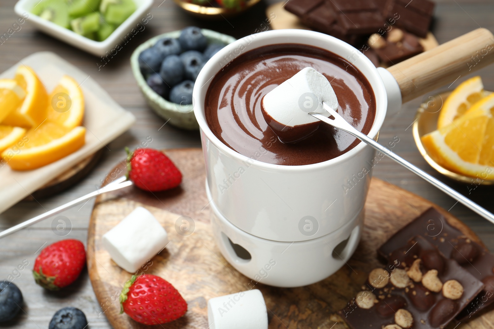 Photo of Dipping sweet marshmallow in fondue pot with melted chocolate at wooden table