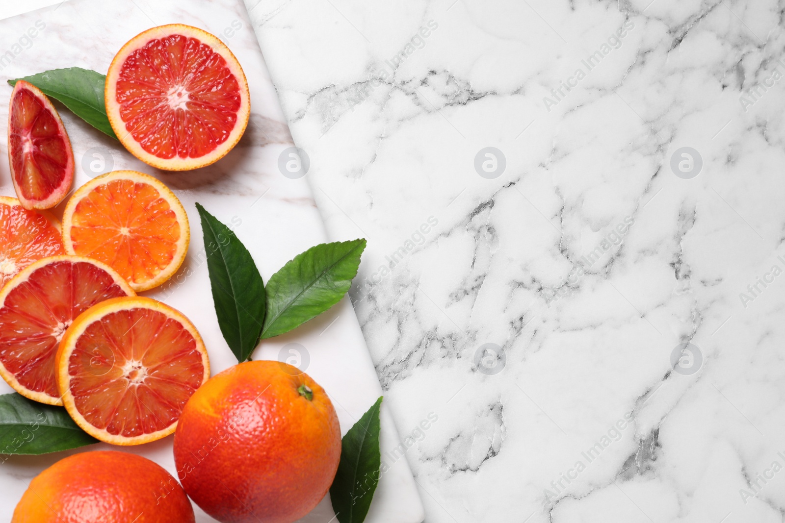 Photo of Whole and cut red oranges on white marble table, top view. Space for text