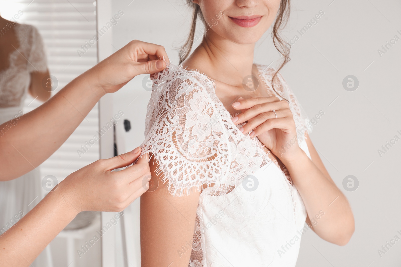 Photo of Woman helping bride to put on wedding dress indoors, closeup